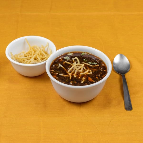 Hot and sour soup with crispy noodles in white bowls, alongside a spoon on a yellow tablecloth.