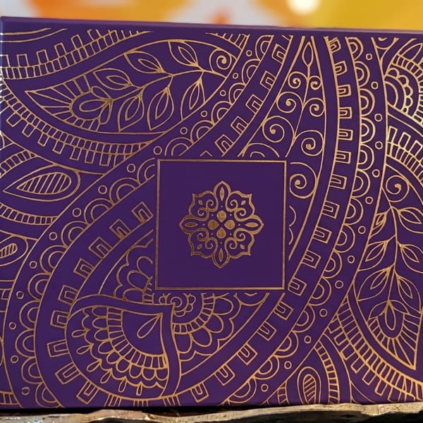 Purple box with intricate gold patterns and a central floral design, on a gold surface.