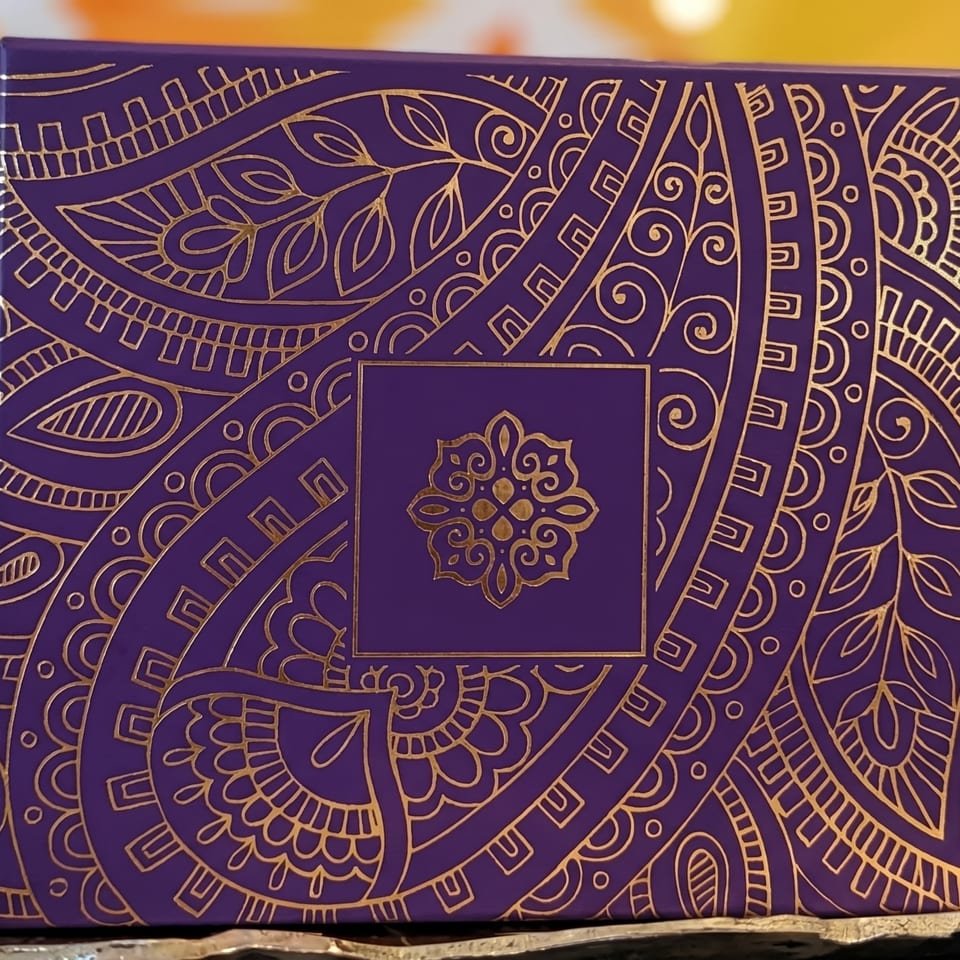 Purple box with intricate gold patterns and a central floral design, on a gold surface.