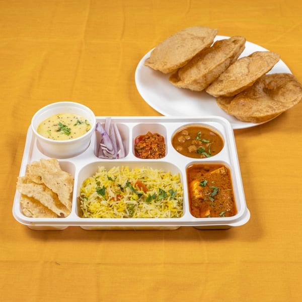 Indian thali with rice, curries, papad, onions, and a plate of puri on a yellow tablecloth.
