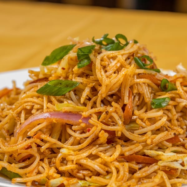 Close-up of spicy noodles with vegetables and green onions on a white plate.