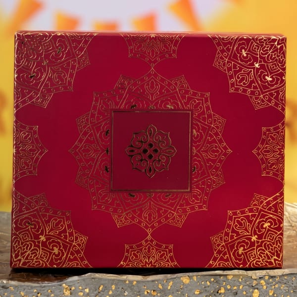 Red box with intricate gold patterns, featuring a central medallion design, on a textured gray surface.