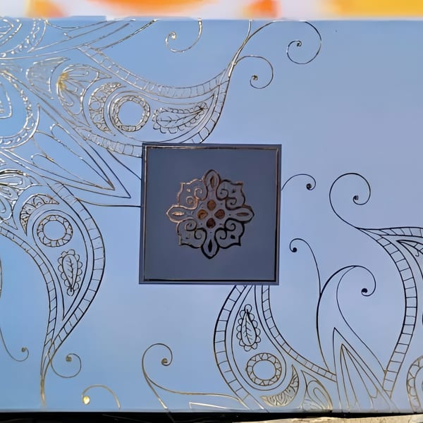 Light blue box with intricate gold and black designs, featuring a central gold medallion.
