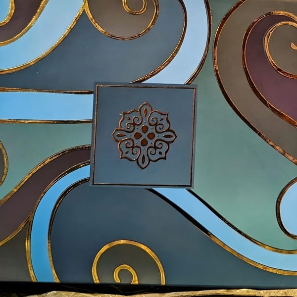 A decorative box with blue, teal, and purple waves outlined in gold, featuring a gold medallion.